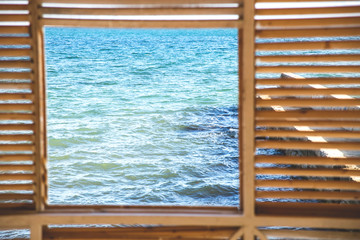 A square window overlooking the sea from a wooden house with cracks. Traveling in nature.