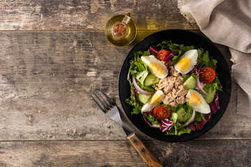 Salad with tuna, egg and vegetables on black plate and wooden table. Top view. Copy space