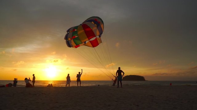 Phuket,Thailand-October,19,2019:mother and father carry a child to take a photo with parasailing  background in golden sunset at Kata beach Phuket Thailand