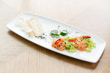 Salmon tartare with cucumber and sesame seeds. Tasting dish on a wooden table.