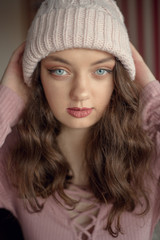 Portrait of cute young woman with blue eyes in a winter warm pink hat waiting for christmas holidays. Peaceful, calm, sad atmosphere.