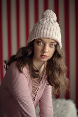 Portrait of cute young woman with blue eyes in a winter warm pink hat waiting for christmas holidays. Peaceful, calm, sad atmosphere.