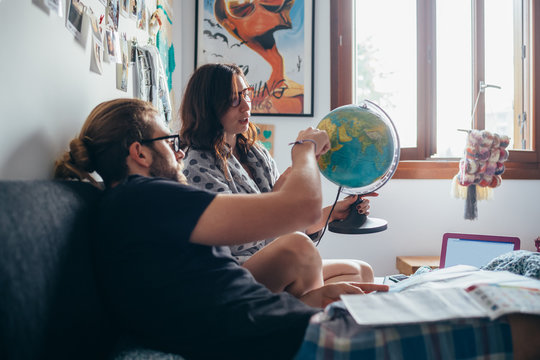 Young Couple Lying On Bed Planning Travel Looking At World Map