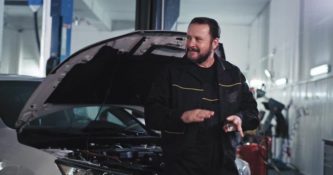 Attractive Mature Man Mechanic In A Modern Auto Service Have A Great Time At Work While Fixing The Car Listening A Good Music From Wireless Headphones And Start To Dancing