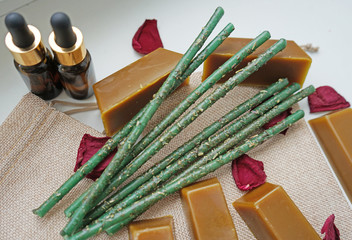 Composition of essential oil bottles, natural wax bars and green handmade herbal candlesticks for...
