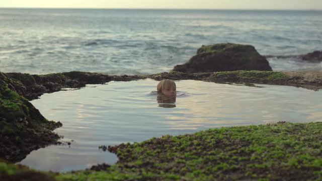 Little boy have fun in a natural little pond with seawater at the Pantai Tegal Wangi beach on the Bali island