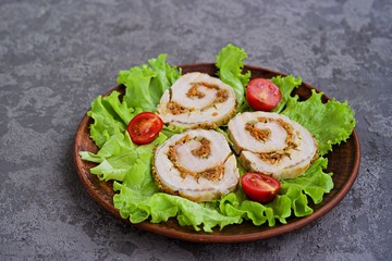 Cold appetizer, sliced baked pork roll with fried carrots and onions on fresh lettuce leaves on a clay plate on a gray concrete background. Holiday recipes meat dishes.