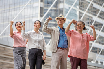 Group of four cheerful asian seniors people Excited and Raised arm up  celebrating a success to travel of retirement trip. power of old man. elder women. ageing society concept. winner. age. fun. city