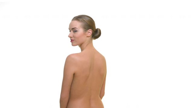 A young naked woman standing with her back to the camera turns and looks into the camera with a smile. Studio portrait on white background.