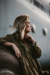 Beautiful woman in green coat standing near the old plane wheel.