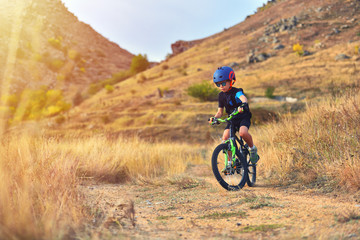 Fototapeta na wymiar Happy kid boy of 7 years having fun in autumn park with a bicycle on beautiful fall day. Active child wearing bike helmet