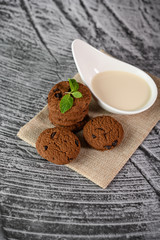 A pile of cookies and a spoon of milk on a cloth on a wooden table