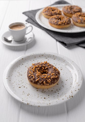 Composition with glazed donuts on a plate on white wooden table.