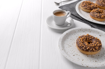 Composition with glazed donuts on a plate on white wooden table.