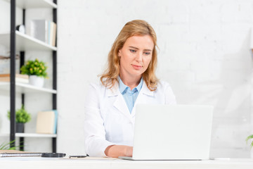 attractive nutritionist sitting at table and using laptop in clinic