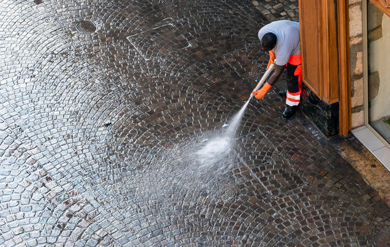 Worker Washing Coblestone Pavemant In Early Morning.