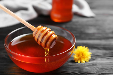 Fototapeta premium Glass bowl with organic honey and dipper on black wooden table, closeup