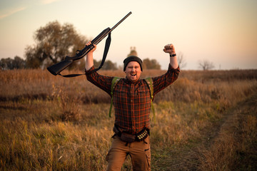 Young irish looking red bearded hunter with shotgun in his hand celebrating successful hunt on the...