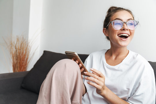 Image of excited woman using cellphone while sitting on sofa