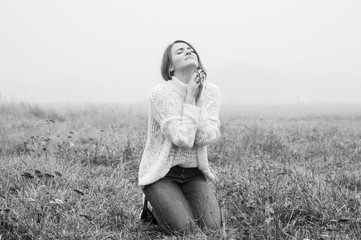 Girl closed her eyes on the knees, praying in a field during beautiful fog. 