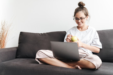 Fototapeta na wymiar Image of smiling attractive woman holding apple and using laptop