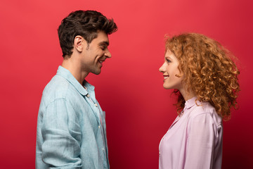 beautiful happy couple in casual clothes looking at each other isolated on red