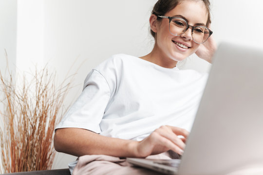 Image of smiling beautiful woman using laptop while sitting on sofa
