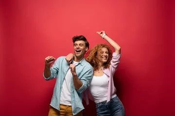 Fotobehang Beautiful excited couple dancing in casual clothes isolated on red © LIGHTFIELD STUDIOS