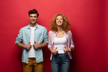 beautiful smiling couple showing thumbs up, isolated on red