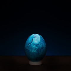 Fototapeta premium Easter egg painted in blue with marble texture on a dark background with backlight