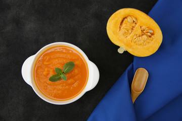 Pumpkin soup in a bowl on a black background with spoon, basil and slice of pumpkin and a fabric napkin with space for text or image. Menu, background, card. Healthy food concept. Top view. Flat lay