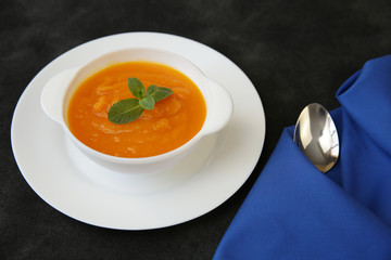 Pumpkin or carrot soup in a bowl on a black background with spoon, basil and a fabric napkin with space for text or image. Menu, background, card. Healthy food concept. Top view. 