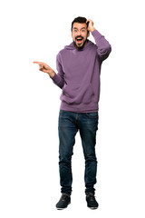 Full-length shot of Handsome man with sweatshirt surprised and pointing finger to the side over...