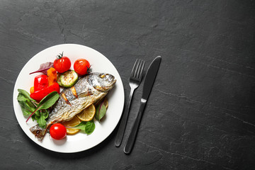 Delicious roasted fish with lemon and vegetables on dark grey table, flat lay. Space for text