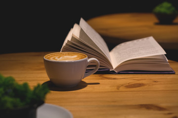 Ceramic cup of cappuccino in coffee shop with pattern on a wooden table with an open book. Latte art. Morning drink. Caffeine.
