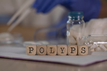 Word POLYPS composed of wooden dices. Pills, documents and a pen in the background.