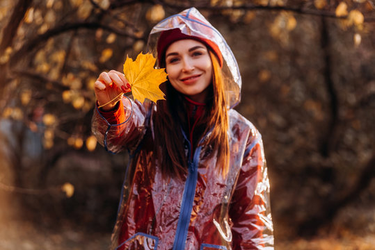 Natural female beauty wearing raincoat holds maple leaves in his hand in autumn