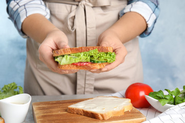 Woman holding tasty fresh sandwich at light grey marble table, closeup