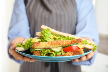 Woman holding plate with tasty sandwiches indoors, closeup