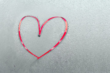 One beautiful bright red heart painted by finger on a frozen blue texture on a glass
