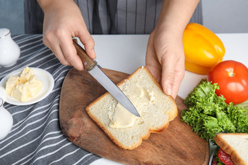 Woman spreading butter on sandwich at white table, closeup