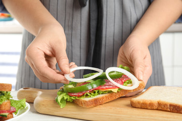 Woman adding onion to tasty sandwich at white wooden table, closeup