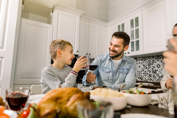 Family Enjoying Thanksgiving Meal At Table. Handsome father and little son clinking glasses with wine and juice and smiling