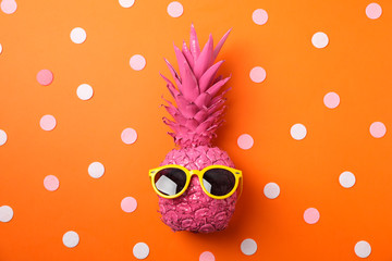 Painted pink pineapple with sunglasses on decorated orange background, space for text