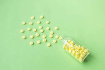 Yellow medical pills scattered from a glass jar on green background with copy space for text. Alternative homeopathy medicine, healthcare and wellness concept. Selective focus