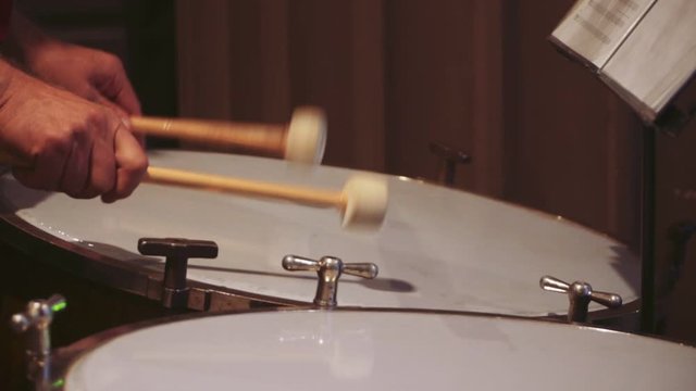 Male hands holding a drum beater beats on the bass drum, beating out the rhythm. Closeup