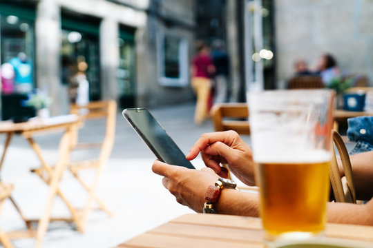 A woman's hand using the mobile phone on the terrace of a bar with a beer