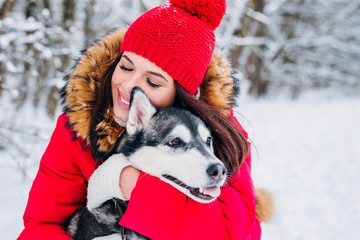 Close-up portrait of young girl huging her husky dog in winter park.