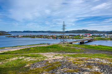 Russia, Arctic, Kola Peninsula, Barents Sea, Teriberka: Road bridge to the oldest part of old Russian settlement small village with fishing boats, old houses, hilly skyline, coastline, power pole.
