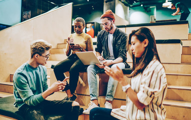 Serious male and female multiracial hipsters ignore real communication using modern gadgets and online chat sitting together in campus, millennial generation diversity crew addicted to smartphones.